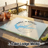 A glass cutting board featuring a blue map of Lake Seminole and a compass rose rests on an outdoor wooden table with copper mugs and lime wedges.