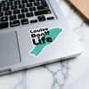 Sticker with "Louise Banff Life" in black text on a turquoise shape on a laptop.