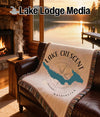 Woven throw blanket with "Lake Crescent Washington" and compass design on leather couch.