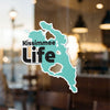 Teal Kissimmee Life sticker on glass, with blurred background details.