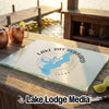 A glass cutting board with a blue Lake Ray Hubbard Texas map graphic rests on a wooden dock beside two copper mugs.