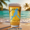 Glass of beer with "Songview Lake" logo and compass on a beach with palm trees.