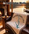 Blanket with Randleman Lake map and compass design on couch by fireplace.