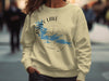Cream sweatshirt with Rainy Lake Minnesota compass graphic and blue lake outline.