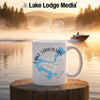 White mug with Lake Lahontan map and compass on a serene lake at sunrise.