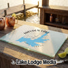 A glass cutting board featuring a blue map of Hayden Lake, Idaho, rests on a wooden table outdoors.