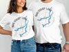 White t-shirts featuring SHUSWAP LAKE map graphic with compass rose and British Columbia text.