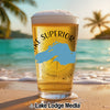 A pint glass filled with beer stands on a sunny tropical beach.