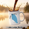 White mug with Lake Mohave and compass graphic, coffee splashing into it.