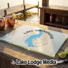 A rectangular glass cutting board featuring a blue Lake Sammamish map graphic rests on a wooden dock outdoors.