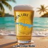 Glass of beer with "Sion Lake" text and compass design on a beach.