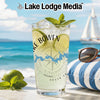 Glass with drink, limes, mint, and compass design on beach background.