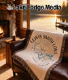 Cream blanket with "Lewis Smith Lake Alabama" text and compass rose design on leather sofa.