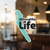 Teal Willoughby Life sticker on glass with blurry background.