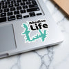 A teal Medina Life sticker is placed on a laptop keyboard.