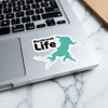 Benbrook Life sticker with teal lake outline on a laptop keyboard.