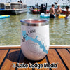A white stemless wine tumbler with a Bass Lake California design sits on a wooden boat deck with people swimming and boating in the background.