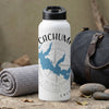 White tumbler with Cachuma map and compass design, next to a rolled towel and duffel bag.