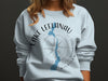 Light blue sweatshirt with "Lake Leelanau Michigan" text, map outline, and compass graphic.