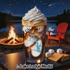 Glass with layered drink and lake map design near campfire and s'mores ingredients.