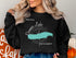 Black sweatshirt with a teal map of Donner Lake and compass rose graphic.
