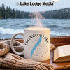 White mug with Greenwood Lake map and compass, next to book and blanket.