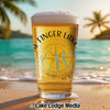 Beer glass with "Finger Lakes New York" and compass design on a beach.