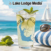 Glass of lemonade with lime and mint on beach with sailboat and sunglasses.