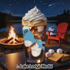 Glass of iced coffee with whipped cream, lake view, campfire, and s'mores ingredients.