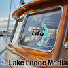 Winnqussam Life logo sticker on a wooden boat window in front of water.