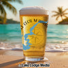 Glass of beer with blue lake outline and compass on a beach.