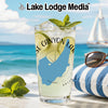 Glass with a drink, lime, mint, sunglasses, and striped pillow on a beach.