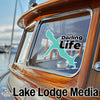 Teal shark sticker and "Darling Life" text on boat window with "Lake Lodge Media" logo.