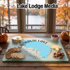 A glass cutting board featuring a map of Garibaldi Lake sits on a wooden table, surrounded by snacks, pumpkins, and a wine glass.