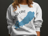 White sweatshirt featuring a blue map of Sand Lake Ontario over a compass rose graphic.