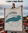 Man holding a woven blanket showing a teal silhouette of Lake Ontario and compass.