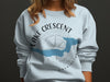 Light blue sweatshirt with "Lake Crescent Washington" in black text and a compass design.