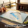 A rectangular glass cutting board with Lake Cachuma, California printed on it sits on a wooden deck.