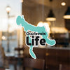 Charlevoix Life sticker in teal shape of Michigan, on a window.