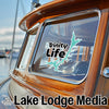 "Trinity Life" decal and "Lake Lodge Media" text on a wooden boat.