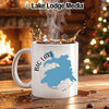 White mug with blue Big Lake Arizona map design, steaming coffee splashing, by fireplace and Christmas tree.