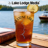 Glass of iced tea with "Bluestone Lake" and compass design on wooden table by lake.