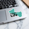 Teal Sylvan Life sticker with black text on a laptop keyboard.