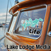 Teal Minnetonka Life sticker and "Lake Lodge Media" text on a wooden boat.