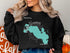 Black sweatshirt with teal Lake Wawasee Indiana map and compass graphic.