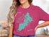 Woman wearing a magenta t-shirt with a turquoise map of Watson Lake.