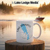 White mug with Lake Winnipeg map and compass design, on a wooden post by a lake.