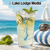 Tall glass with drink, lime, mint, and compass graphic on a beach.