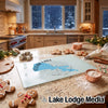 A glass cutting board featuring a blue map of Clear Lake California and compass design rests on a kitchen counter surrounded by gingerbread cookies, flour, and baking supplies.