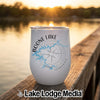 A white stainless steel wine tumbler with a Boone Lake Tennessee map and compass design sits on a wooden dock at sunset.